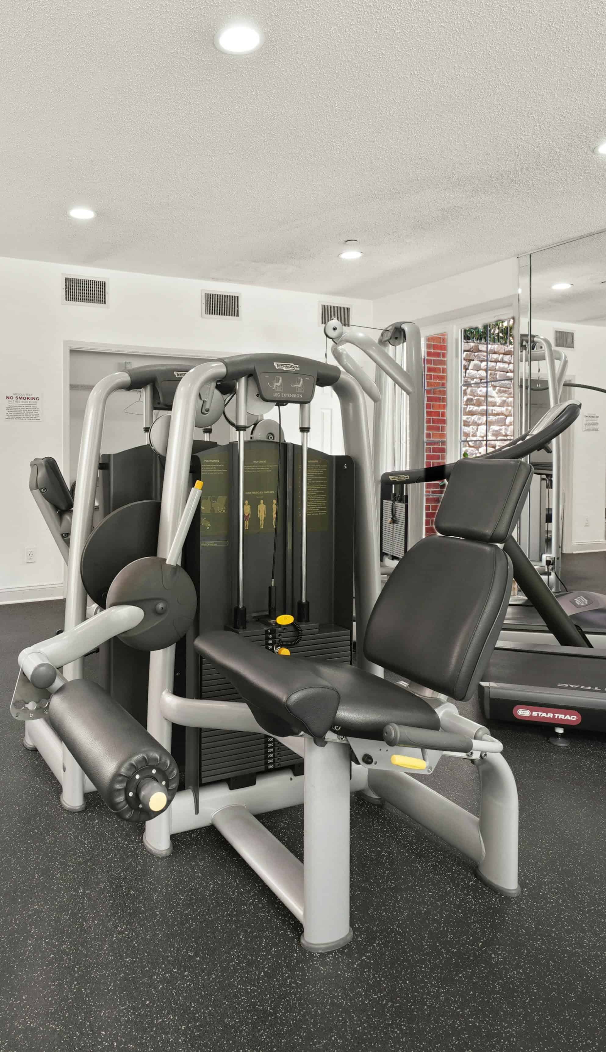 Equipamento de musculação multifuncional com estrutura cinza e assentos pretos em academia
